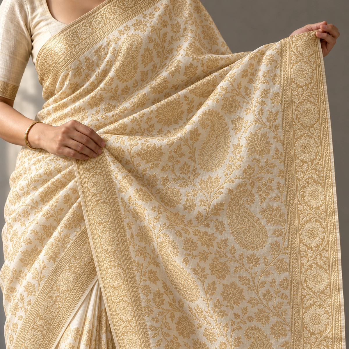 An ivory and gold Banarasi-style brocade saree held open to show dense woven floral patterning